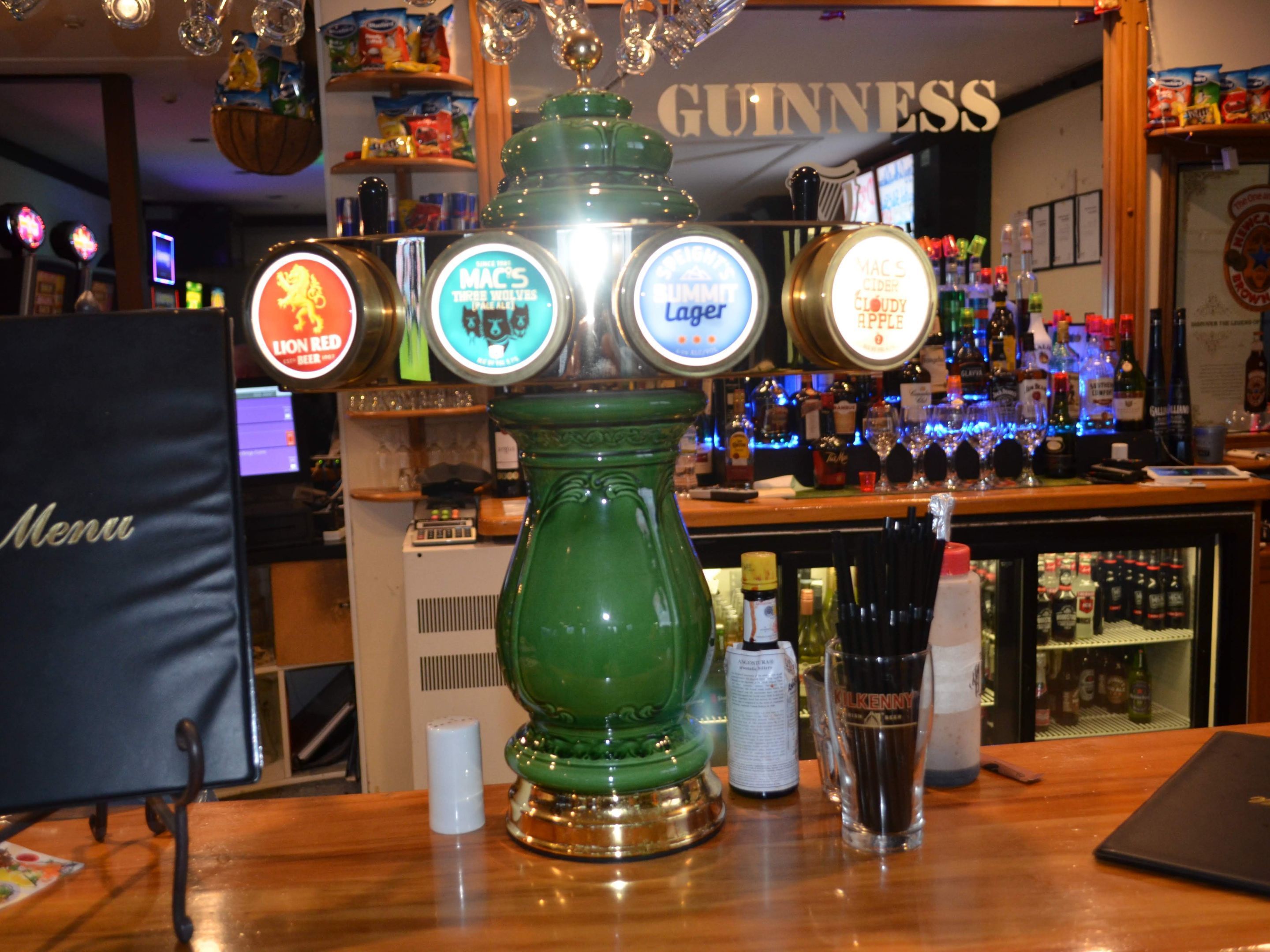Um bar com um mostrador de torneiras de cerveja verde e um suporte para cardápio.