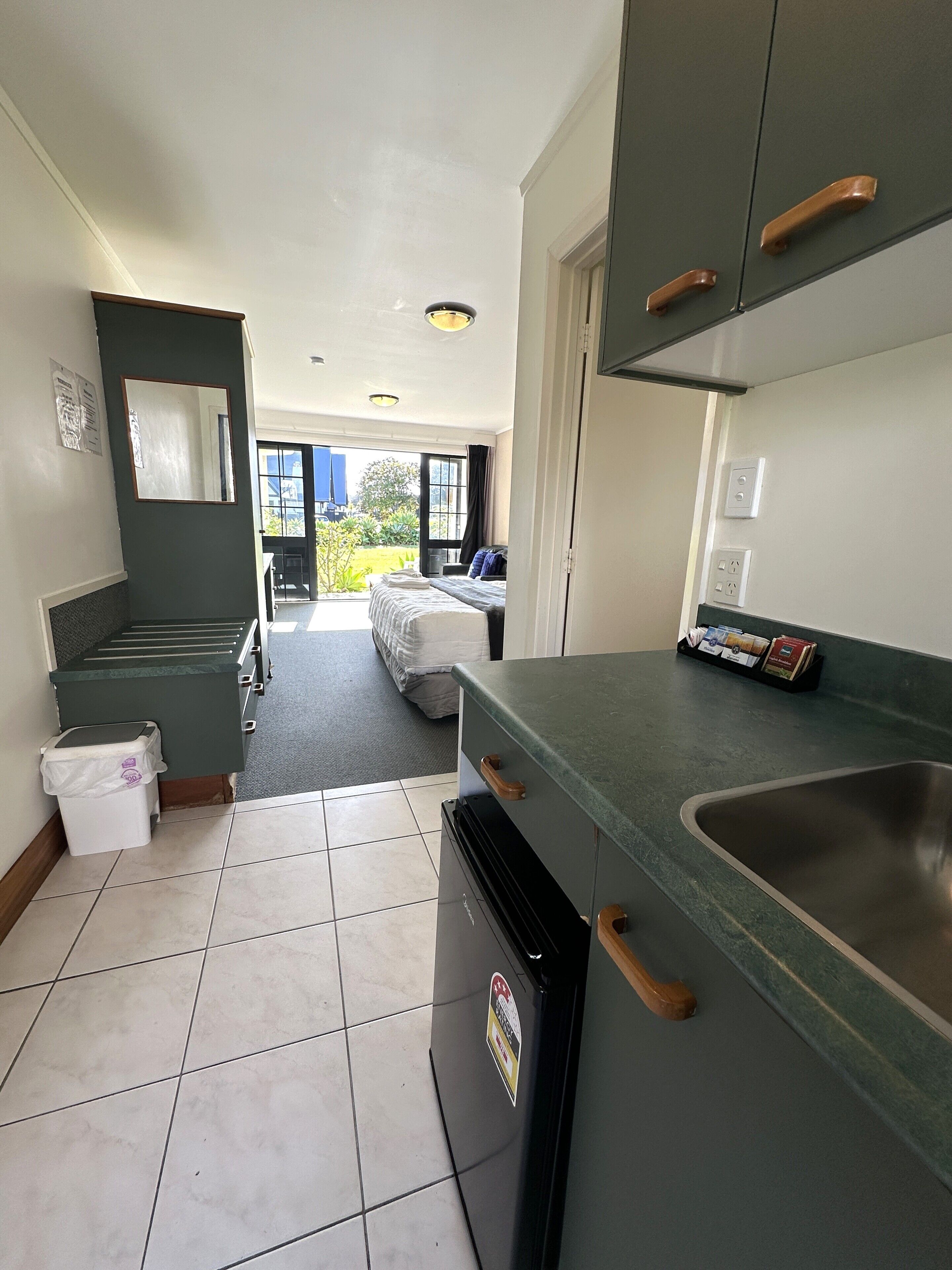 A kitchen with a refrigerator, a sink, and a window overlooking a garden.
