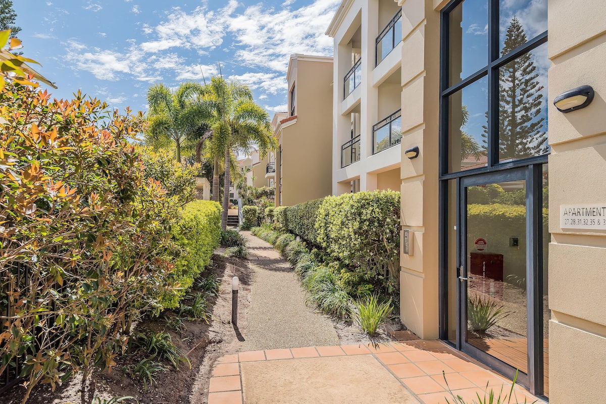 A pathway leading to a building with a sign indicating apartments numbered 27, 28, 31, 32, 35, and 36.