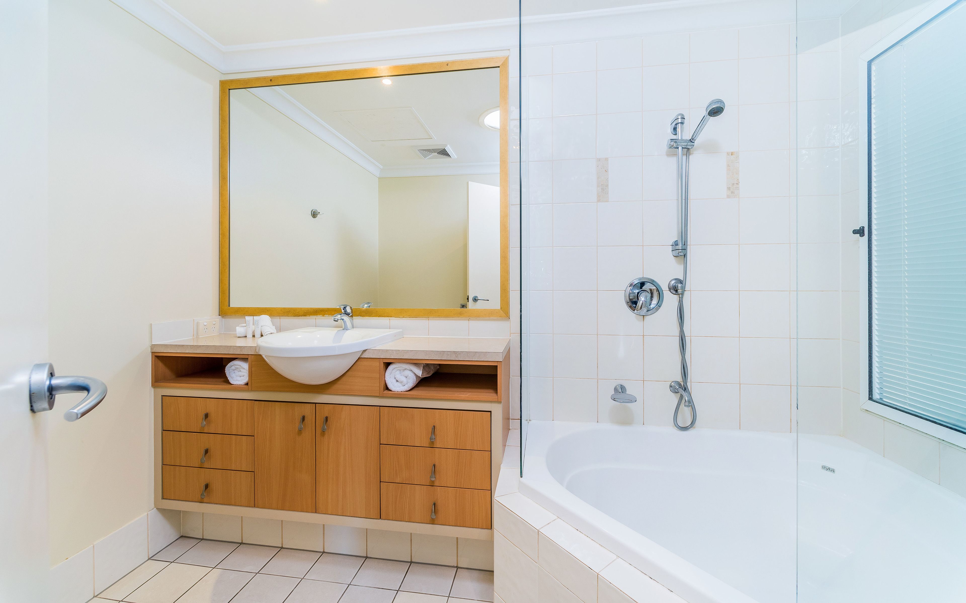 A modern bathroom with a large mirror, a sink, wooden cabinets, and a bathtub.