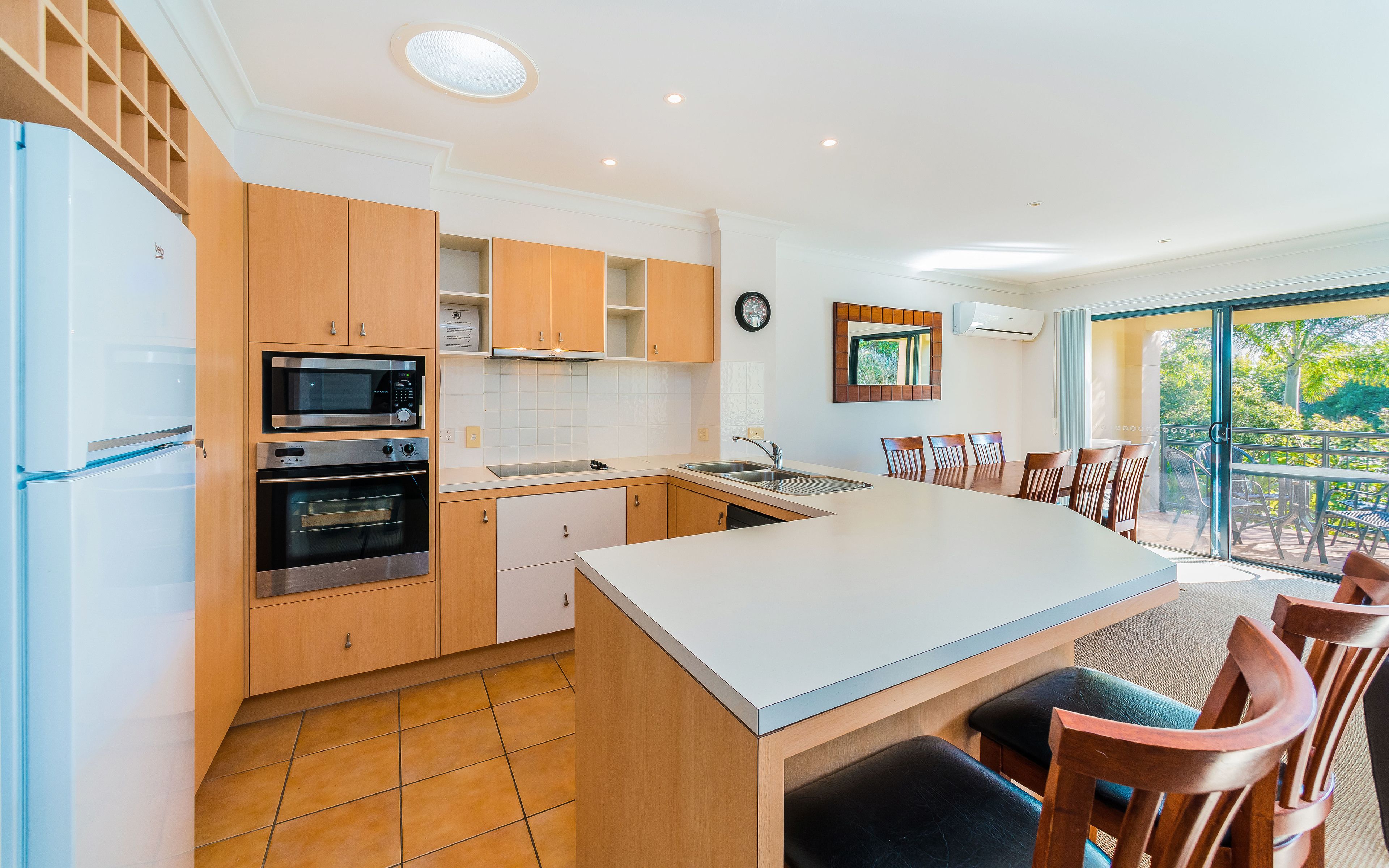A modern kitchen with wooden cabinets, a built-in oven, a microwave, and a large island with seating.