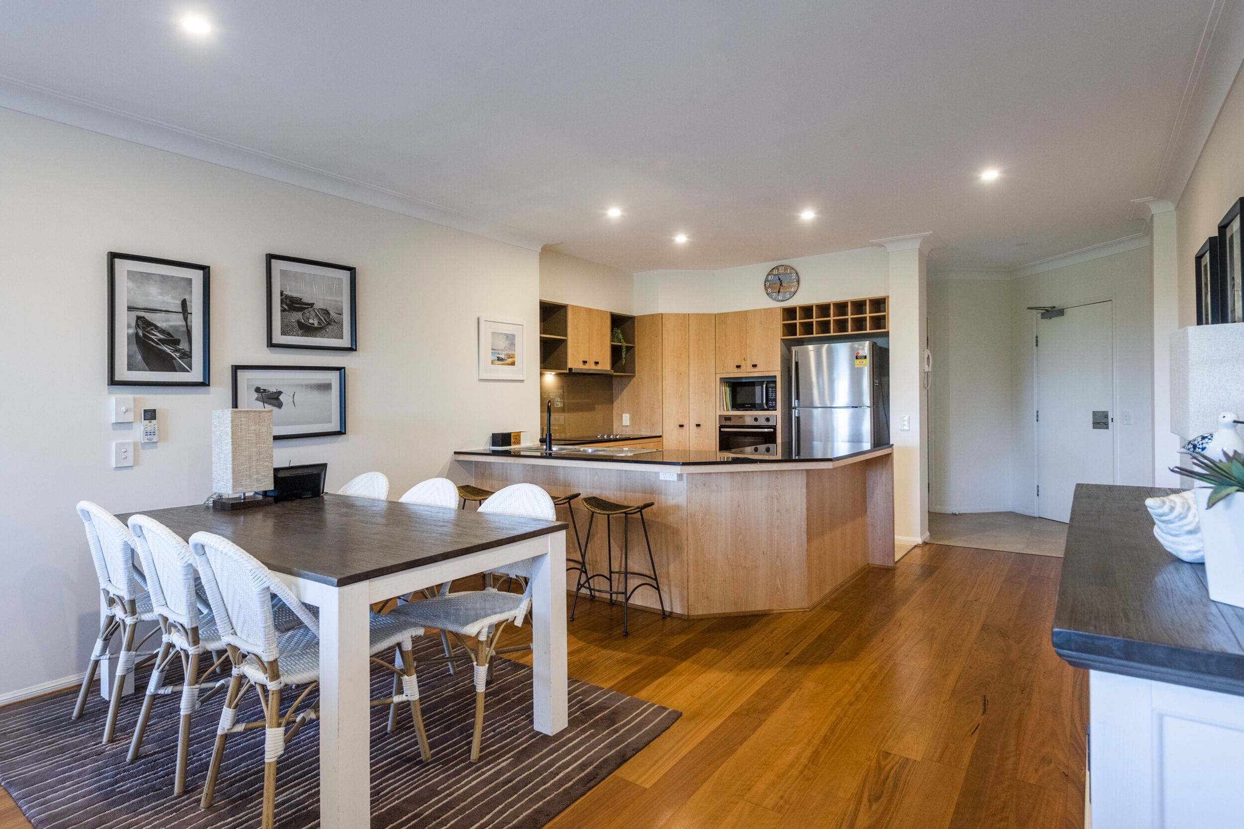 A modern kitchen with wooden cabinets, a central island, and a dining area with white chairs.