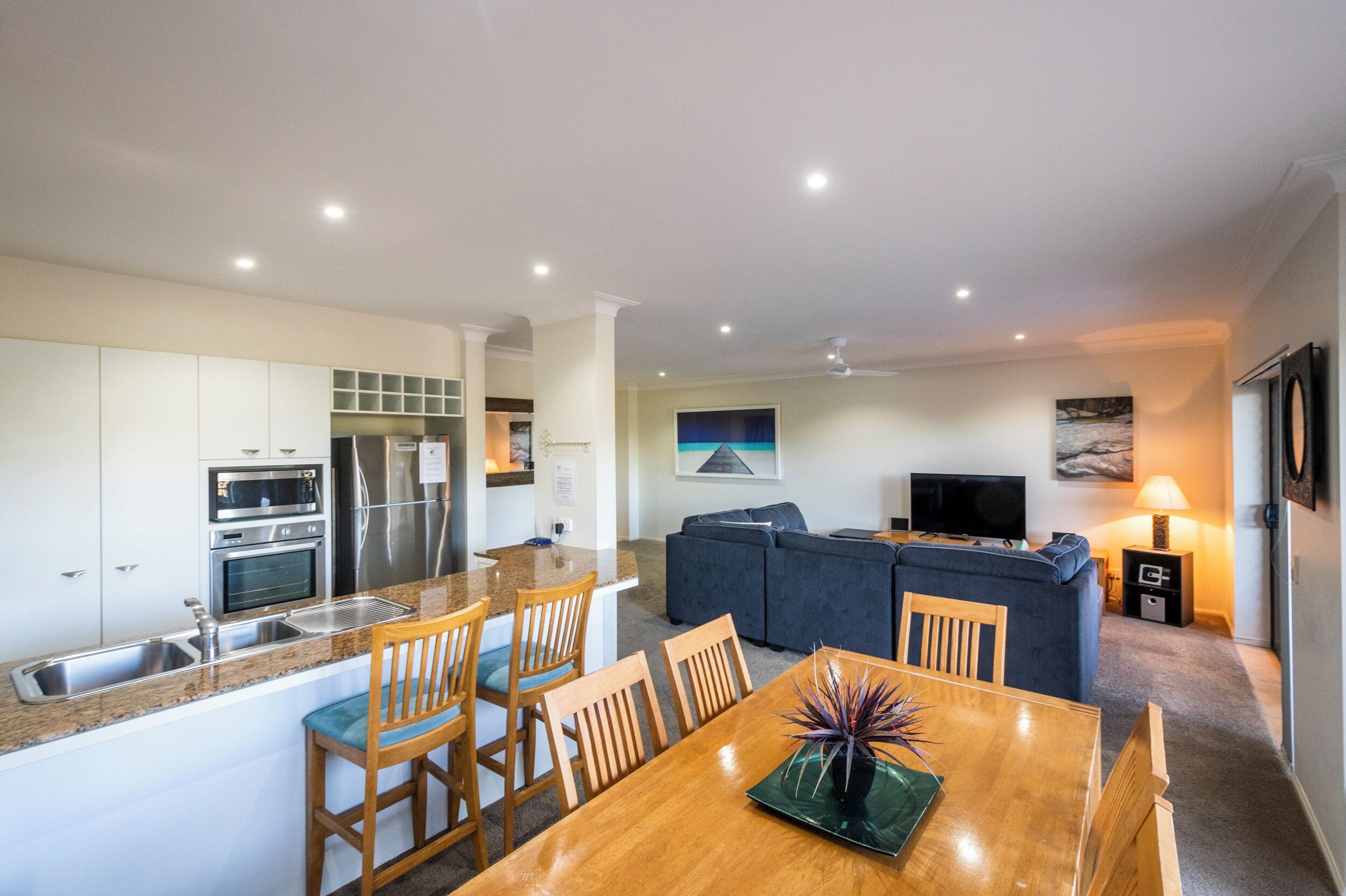 A modern kitchen with a dining area, a living room with a sofa and TV, and a small entertainment unit.