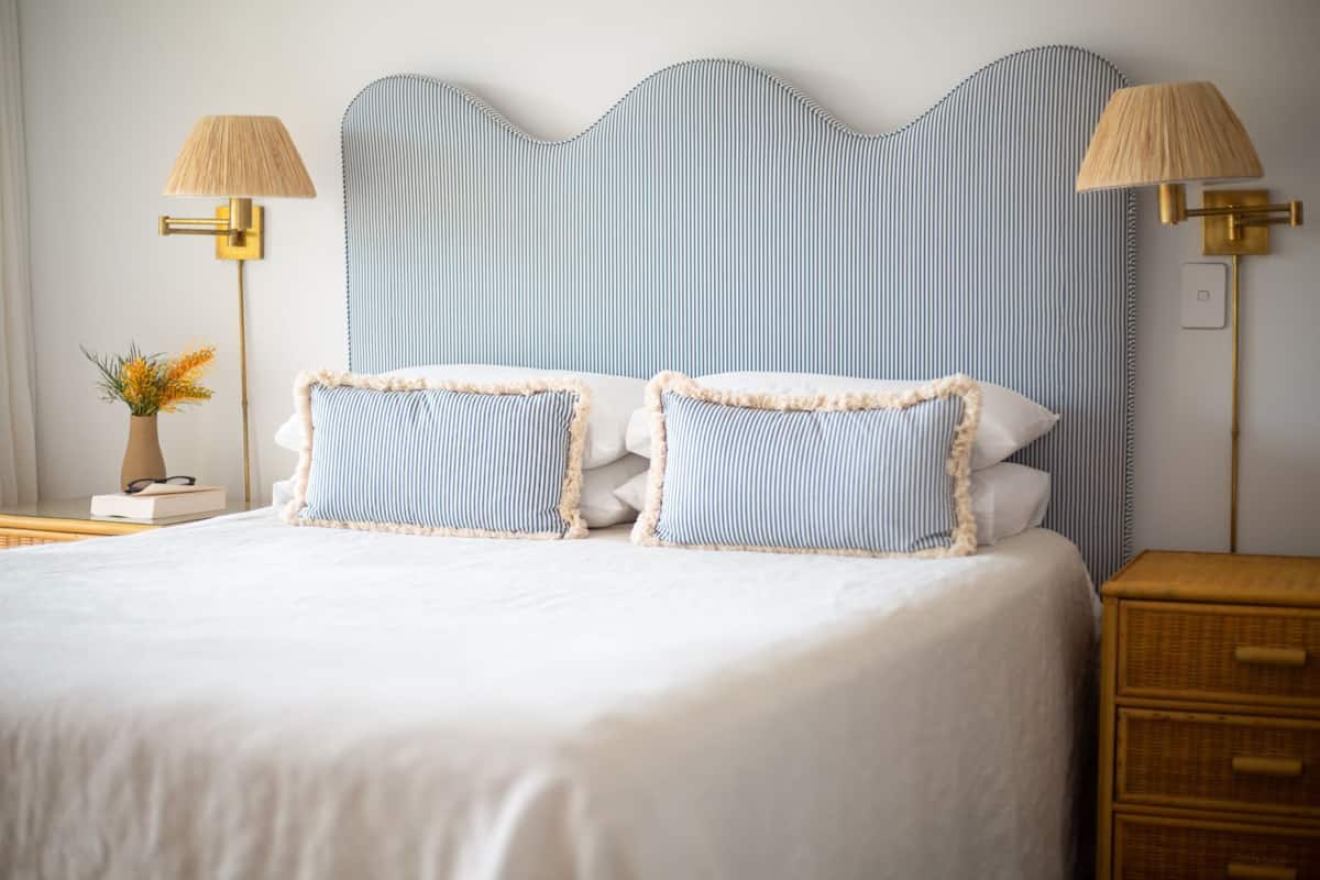 A neatly made bed with striped pillows and two wall-mounted lamps.