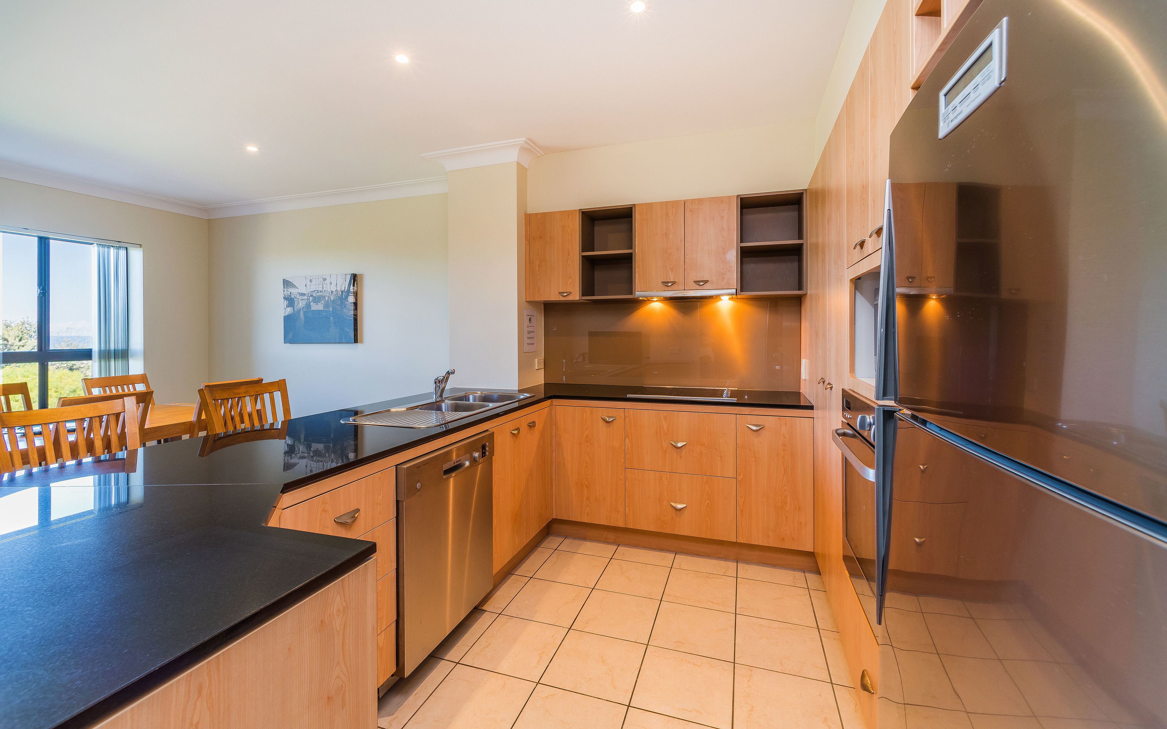 A modern kitchen with wooden cabinets, a black countertop, and a stainless steel refrigerator.
