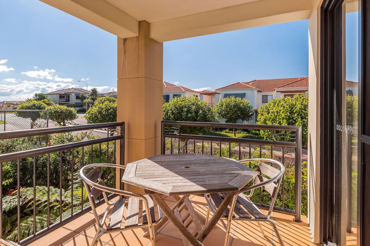 A balcony with a wooden table and chairs, a metal railing, and a view of neighboring houses.