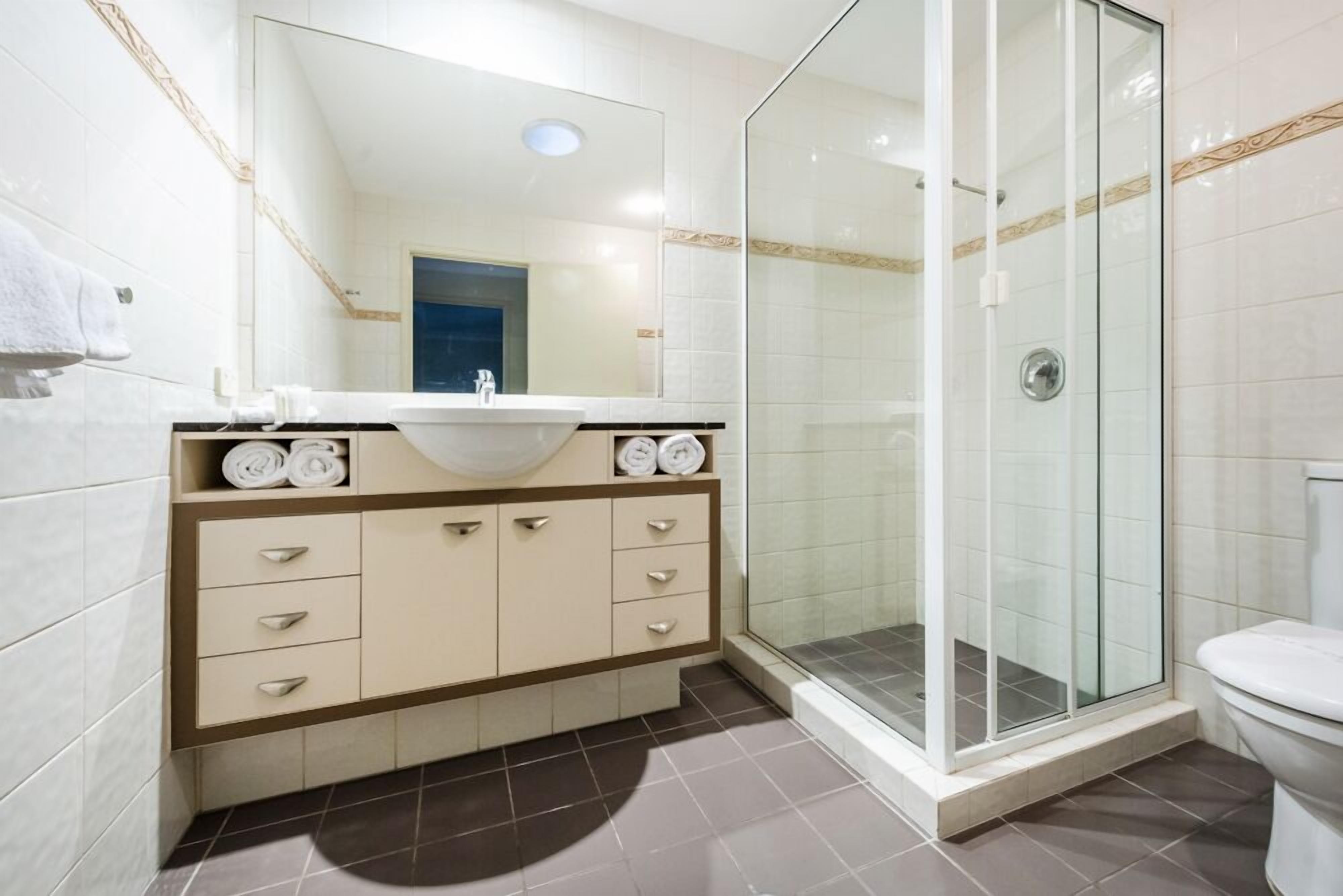 A modern bathroom with a glass shower enclosure, a white sink, and a beige vanity with drawers.
