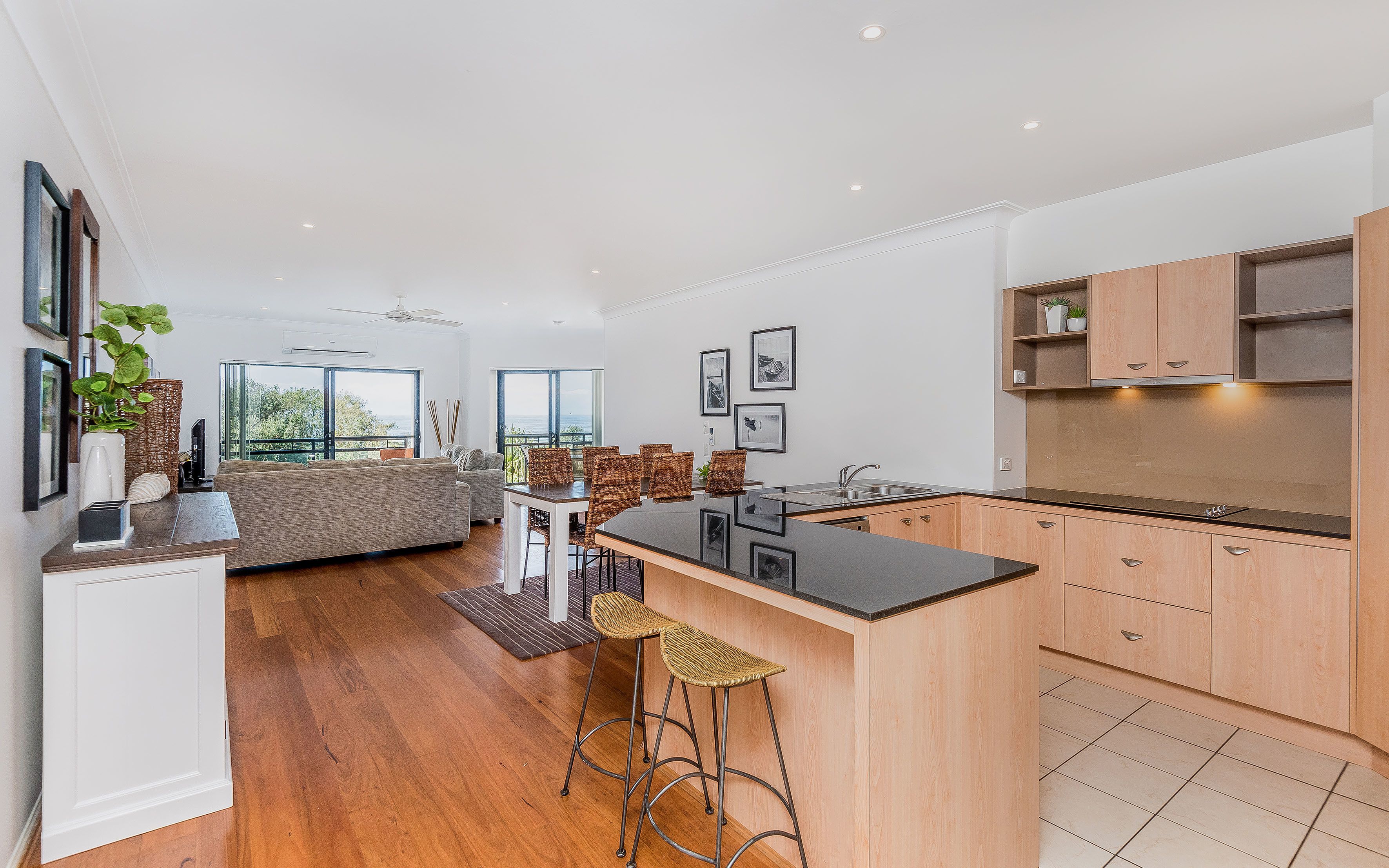 Une cuisine moderne avec des meubles en bois, un îlot central et un coin repas doté de chaises en osier.