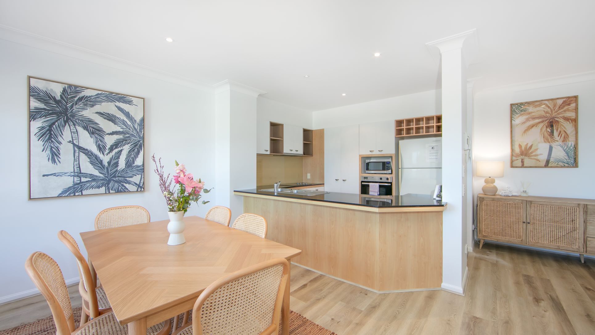 Een moderne keuken met een centraal eiland, houten kasten en een eethoek met een tafel en stoelen.