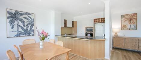 Een moderne keuken met een centraal eiland, houten kasten en een eethoek met een tafel en stoelen.
