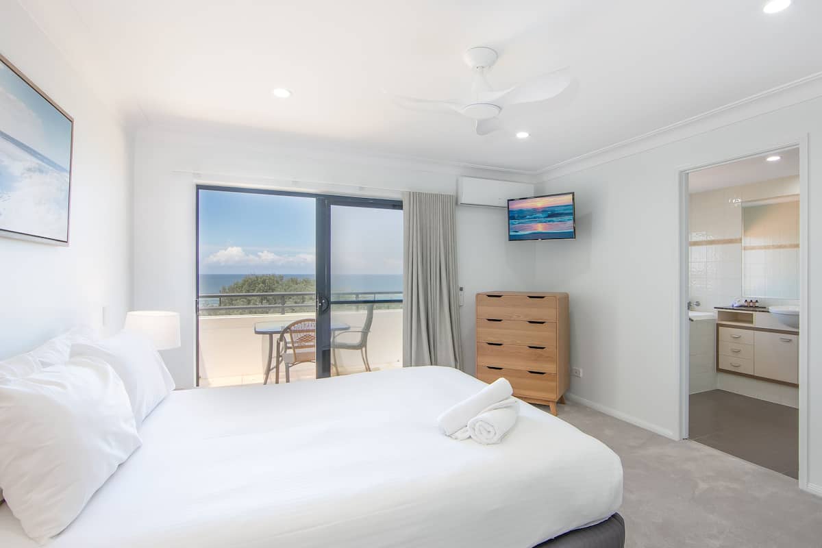 A hotel room with a bed, a TV, a balcony with a view, and a bathroom.