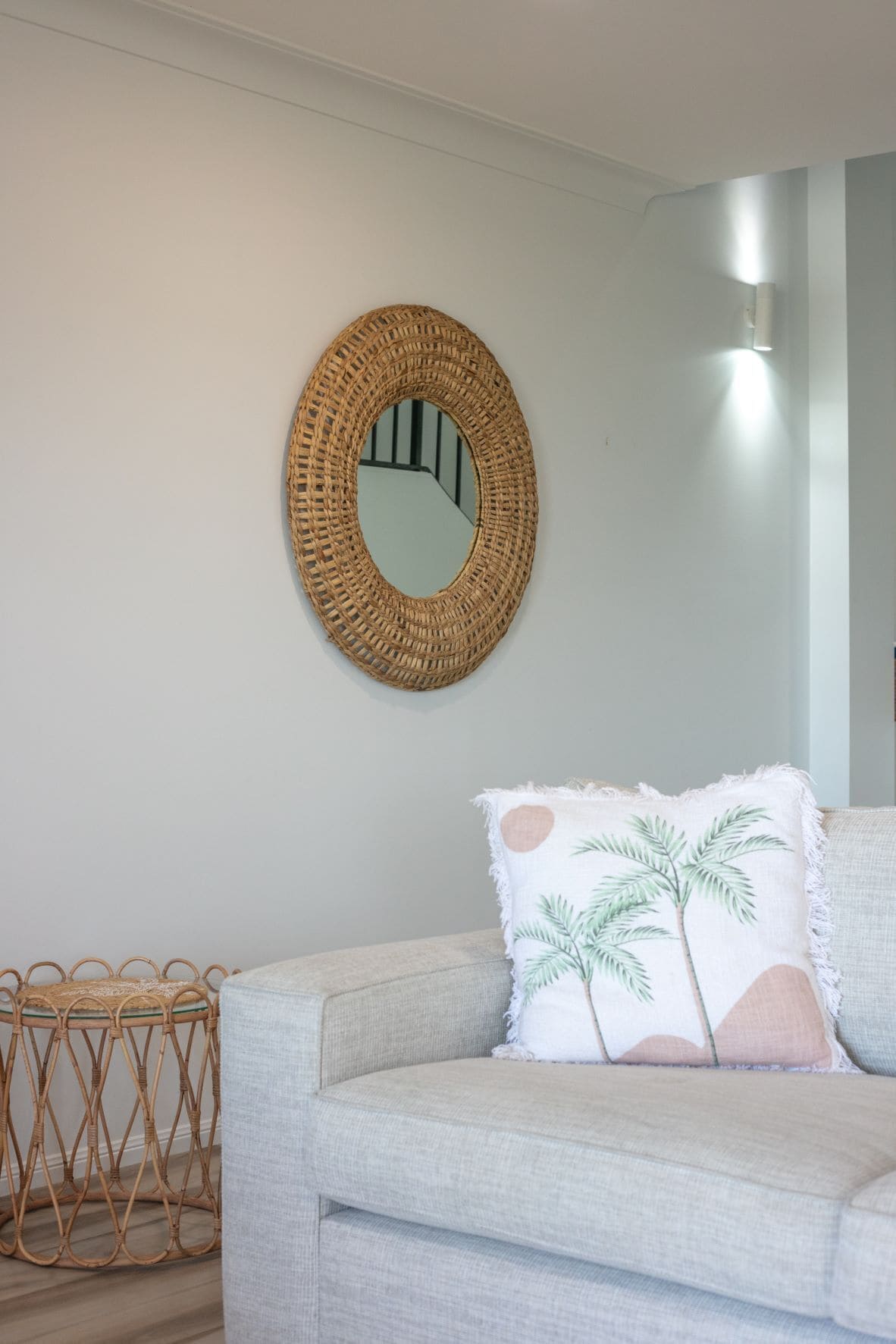 A room with a light grey sofa, a woven mirror, and a rattan side table.