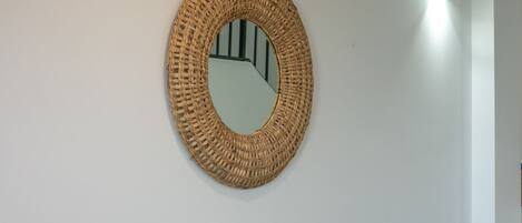 Una habitación con un sofá de gris claro, un espejo tejido y una mesita de ratán.