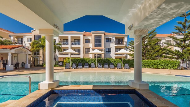 Zona de piscina con vista despejada, sillas de descanso y un edificio con balcones al fondo.