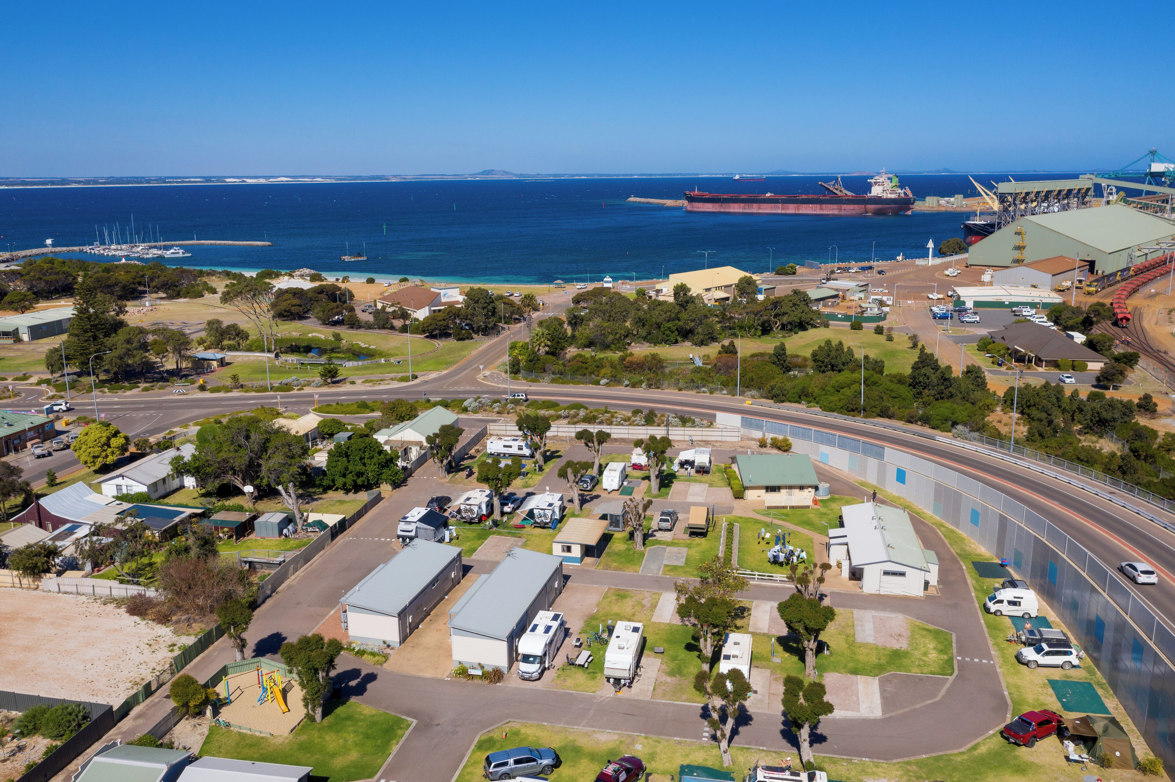Vue aérienne d’une zone côtière comprenant un port de plaisance, un grand navire de transport de marchandises et une voie ferrée.