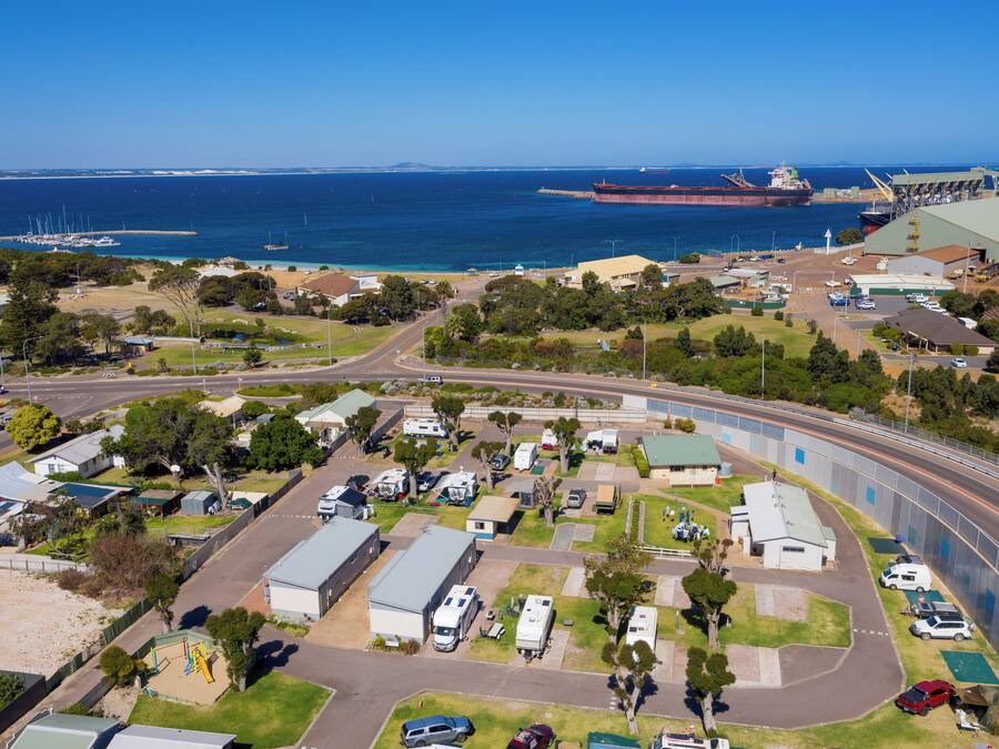 Vue aérienne d’une zone côtière comprenant un port de plaisance, un grand navire de transport de marchandises et une voie ferrée.