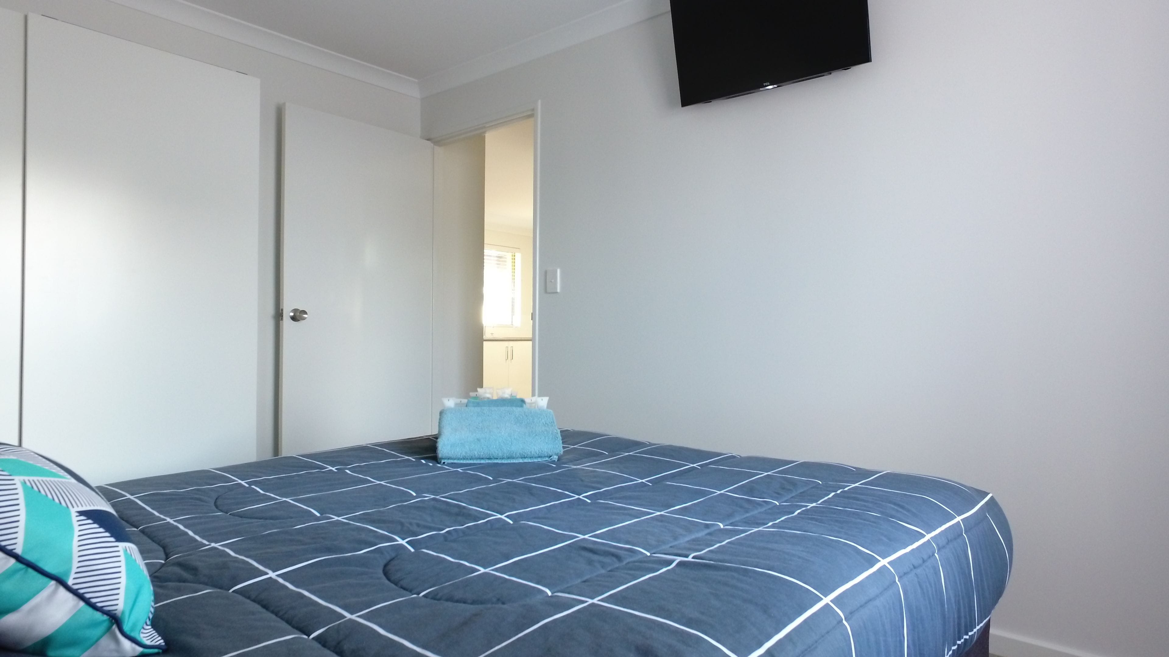 A bedroom with a bed, a wardrobe, and a television on the wall.