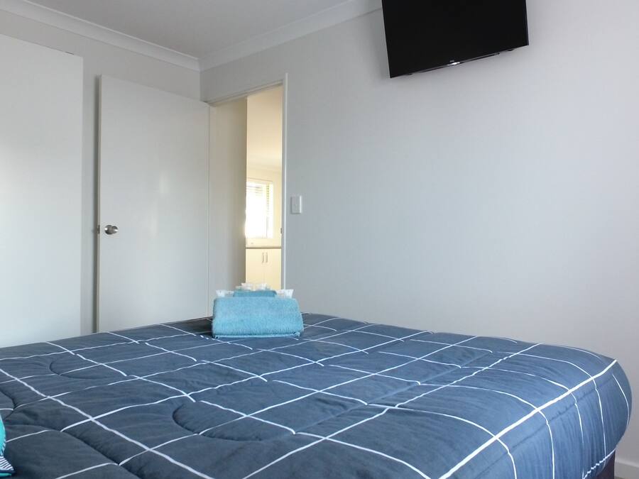 A bedroom with a bed, a wardrobe, and a television on the wall.