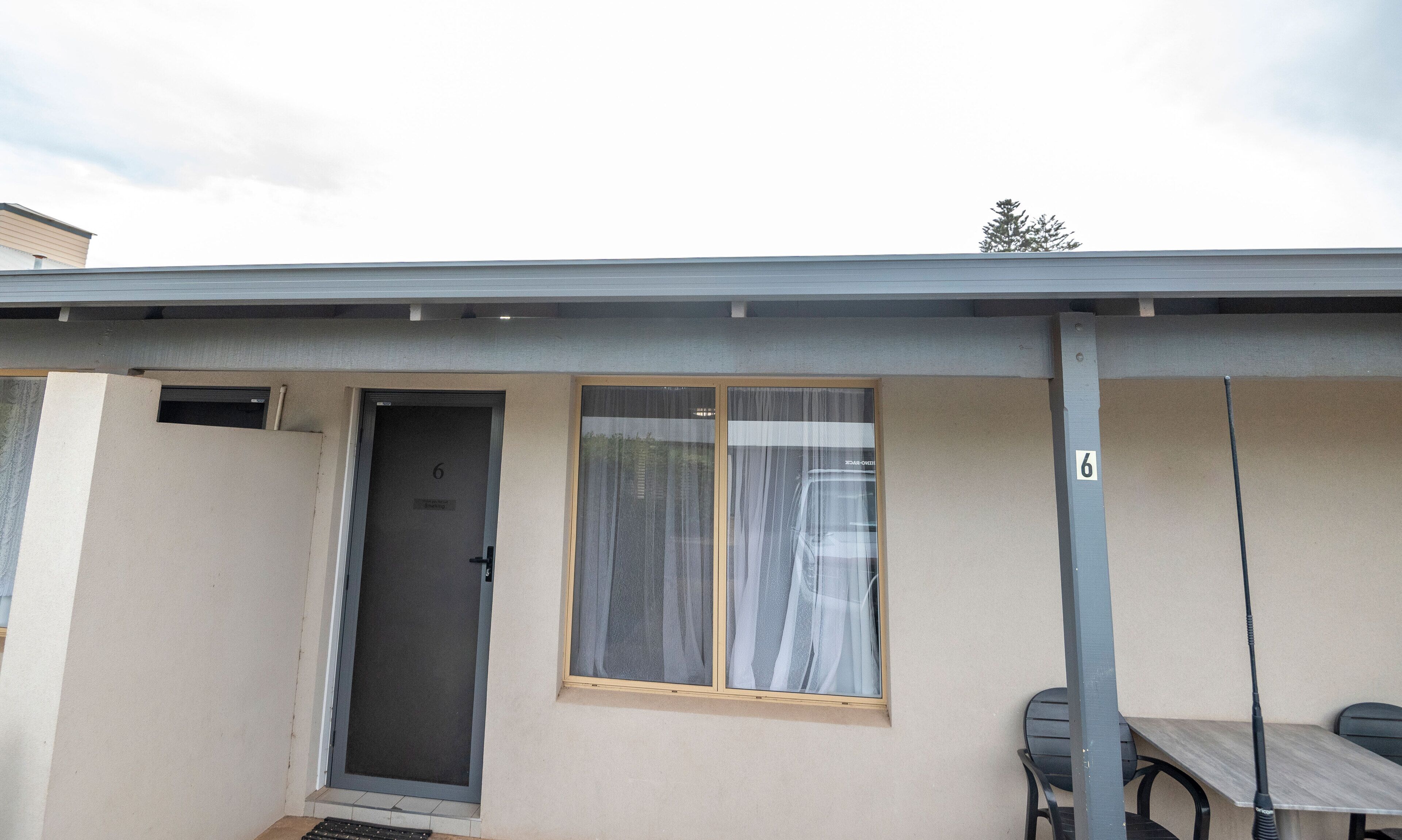 Um edifício com porta numerada, janela com cortinas e mesa com cadeiras na parte externa.