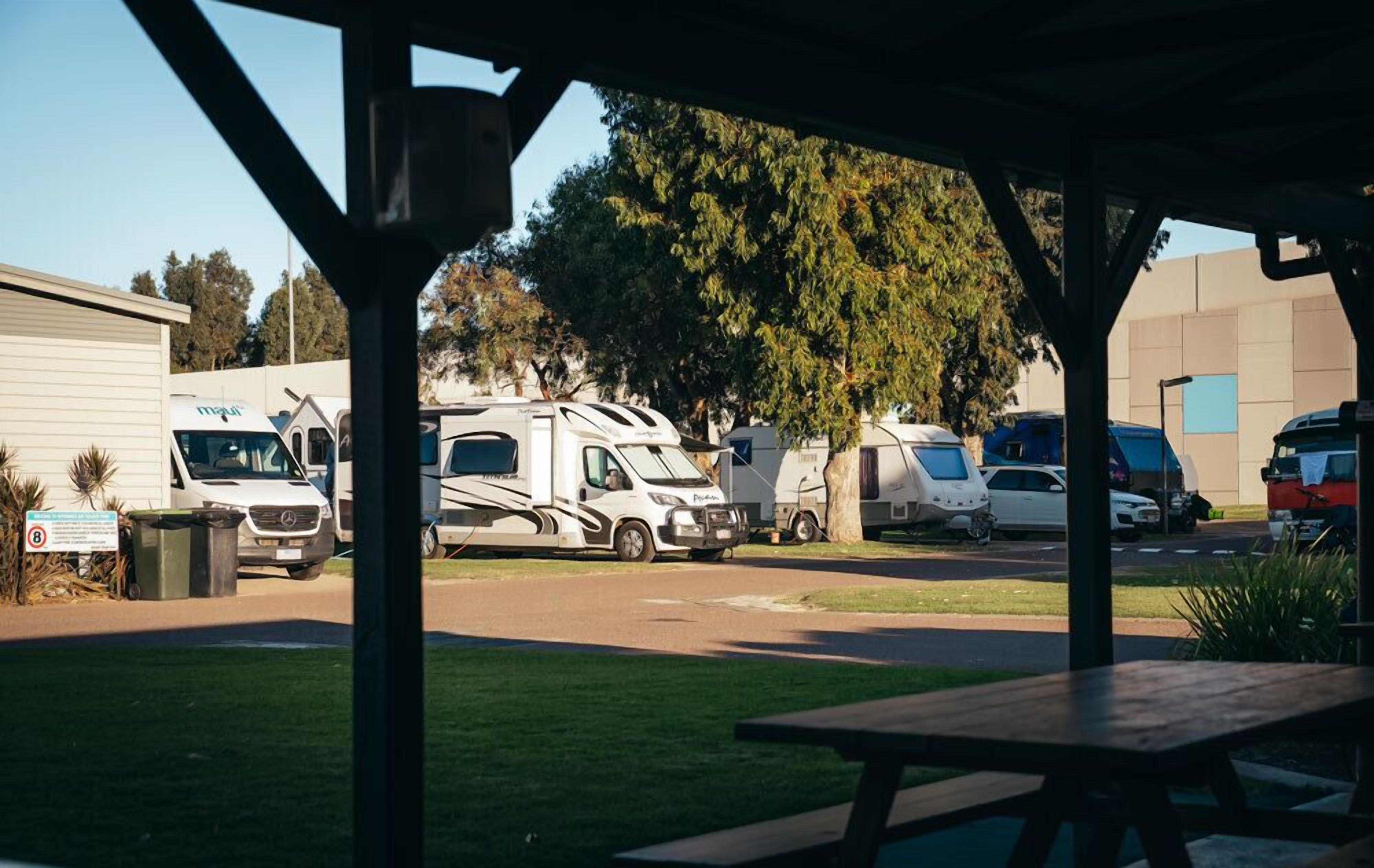 Un'area parcheggio con camper e automobili, un tavolo da picnic e un edificio con un cartello.