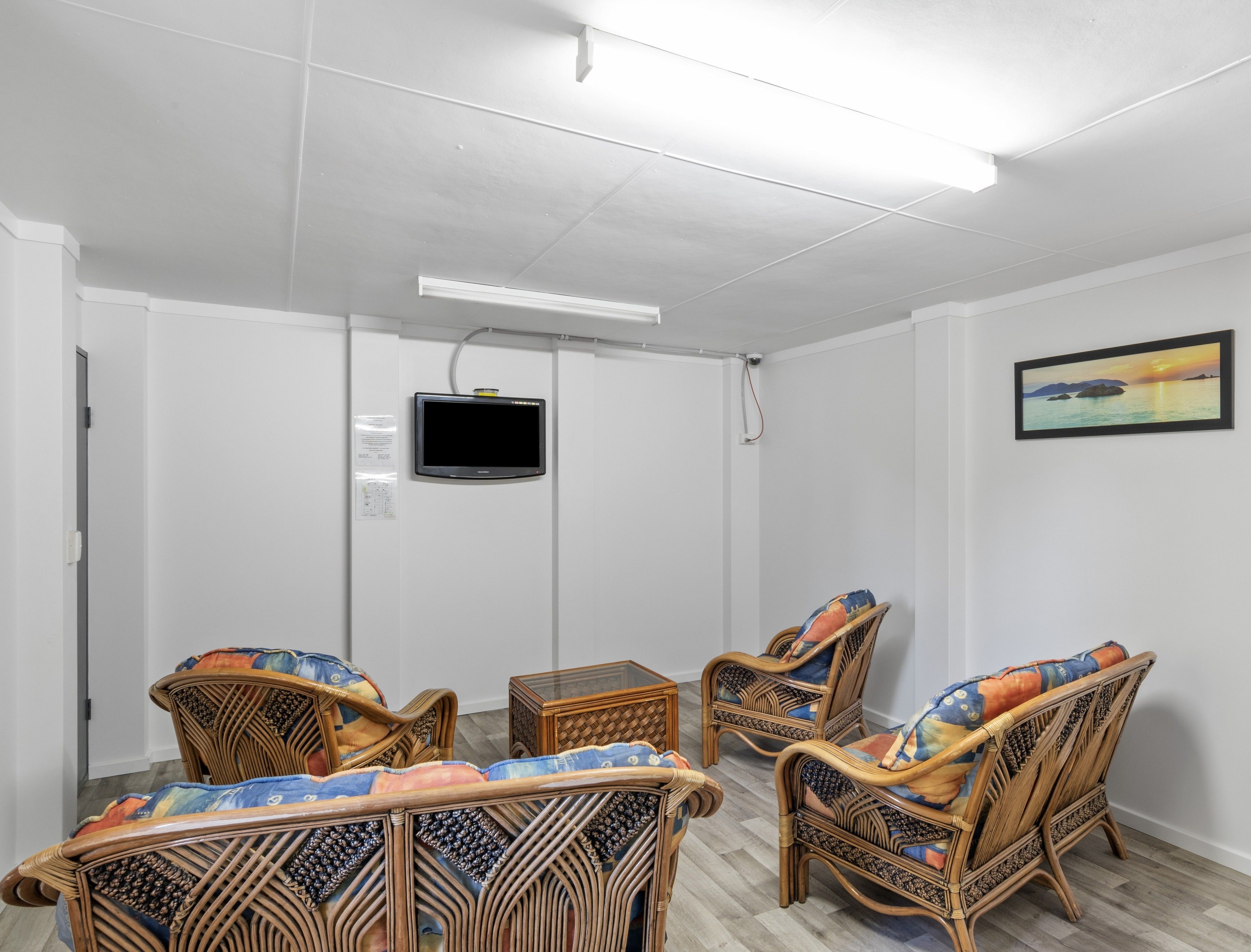 A room with white walls, a flat-screen TV mounted on the wall, and wicker furniture with colorful cushions.