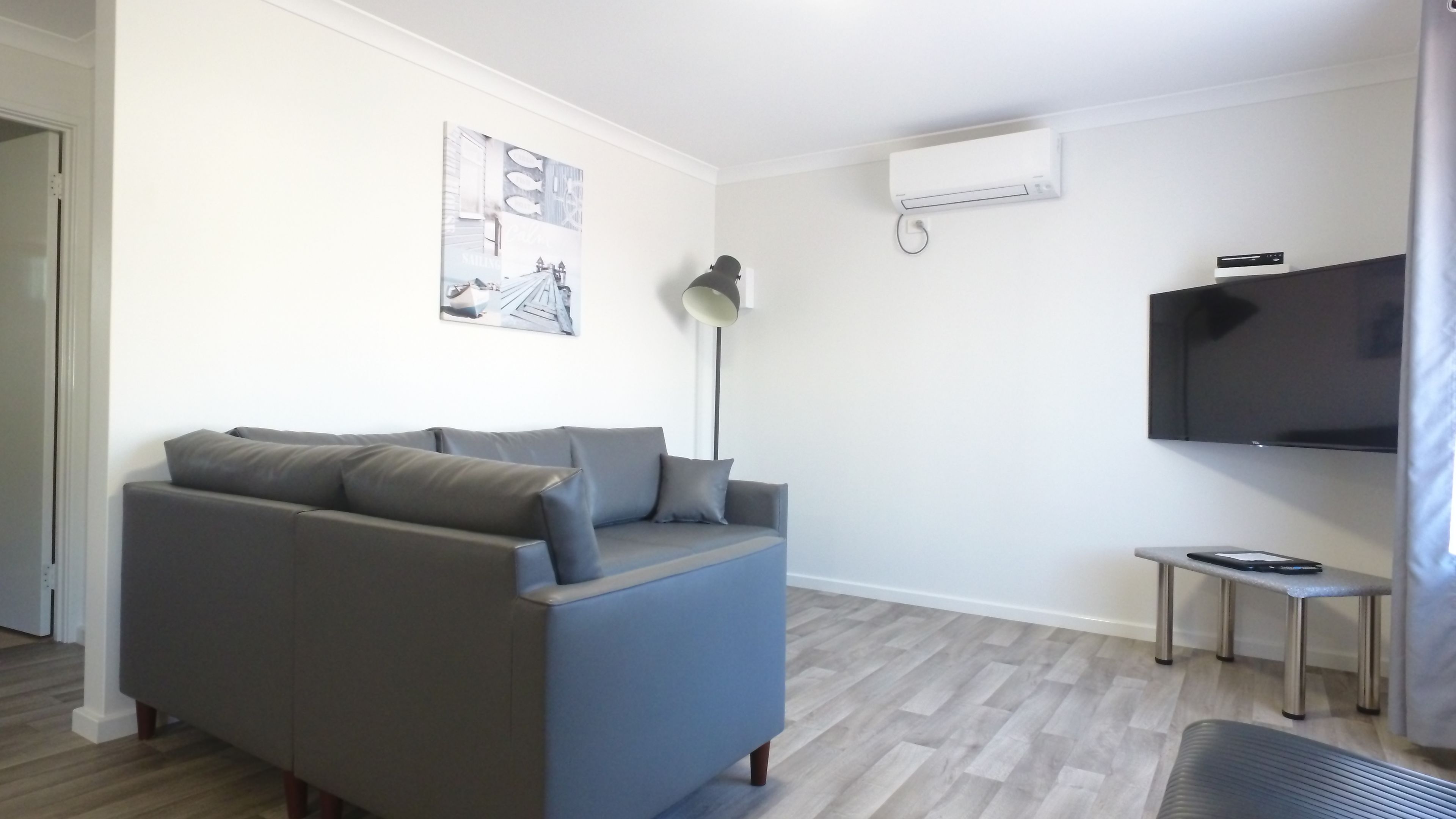 A modern living room with a grey sofa, a flat-screen TV mounted on the wall, a small side table, and a floor lamp.