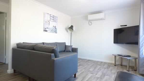Una sala de estar moderna con un sofá gris, un televisor de pantalla plana montado en la pared, una mesita auxiliar y una lámpara de pie.