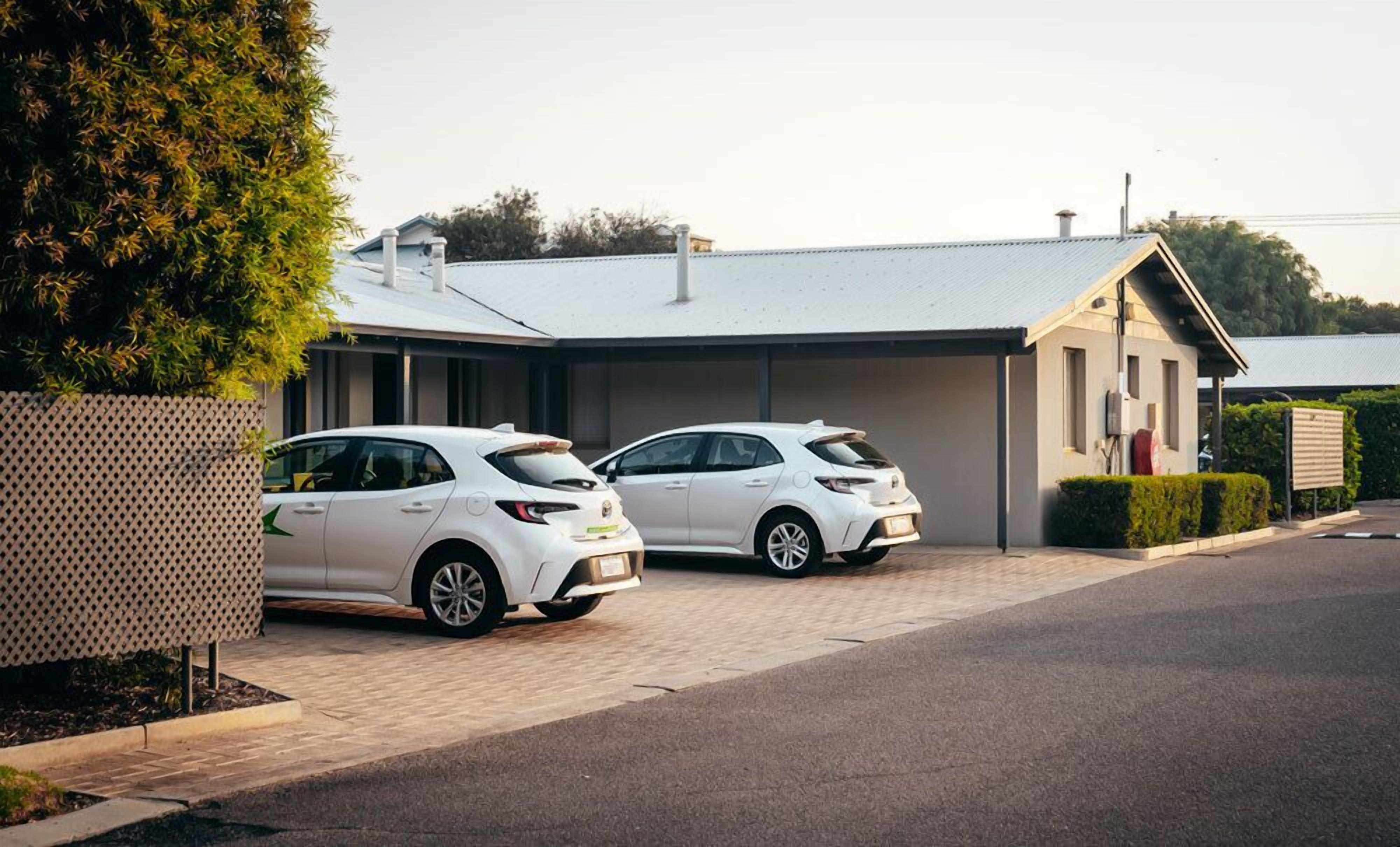 Dos coches blancos estacionados frente a una casa moderna con garaje.