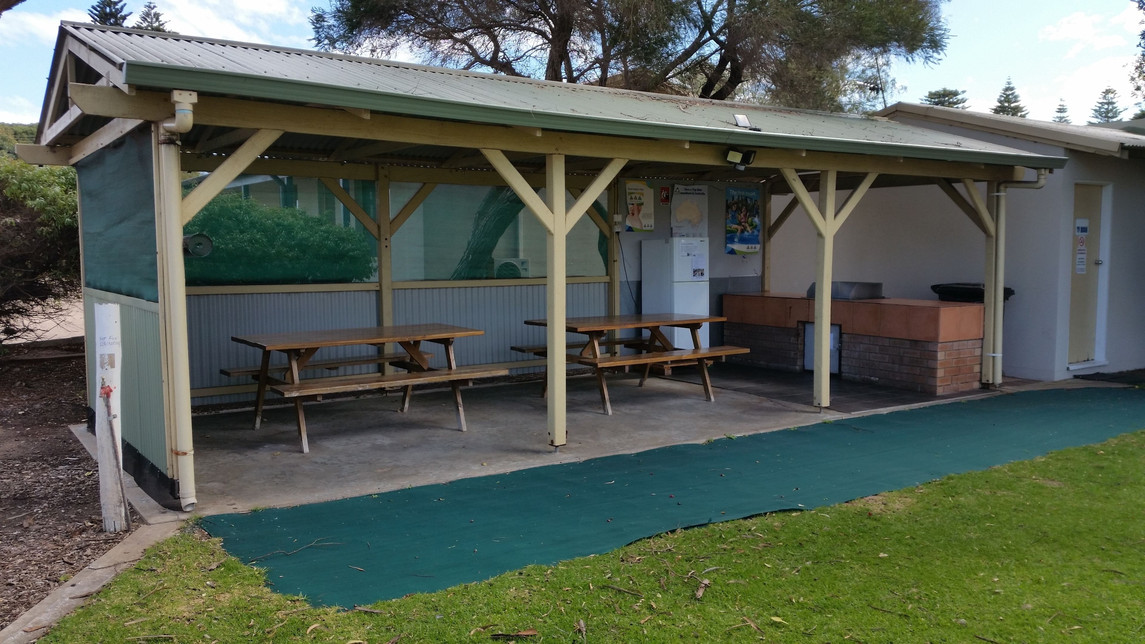 A covered picnic area with picnic tables and a barbecue grill.