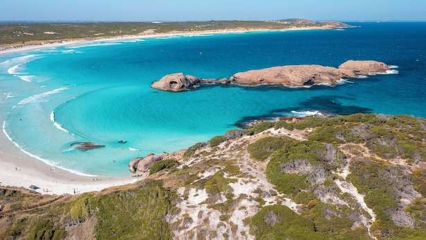 Un paisaje costero con aguas turquesas cristalinas, formaciones rocosas y una playa arenosa.