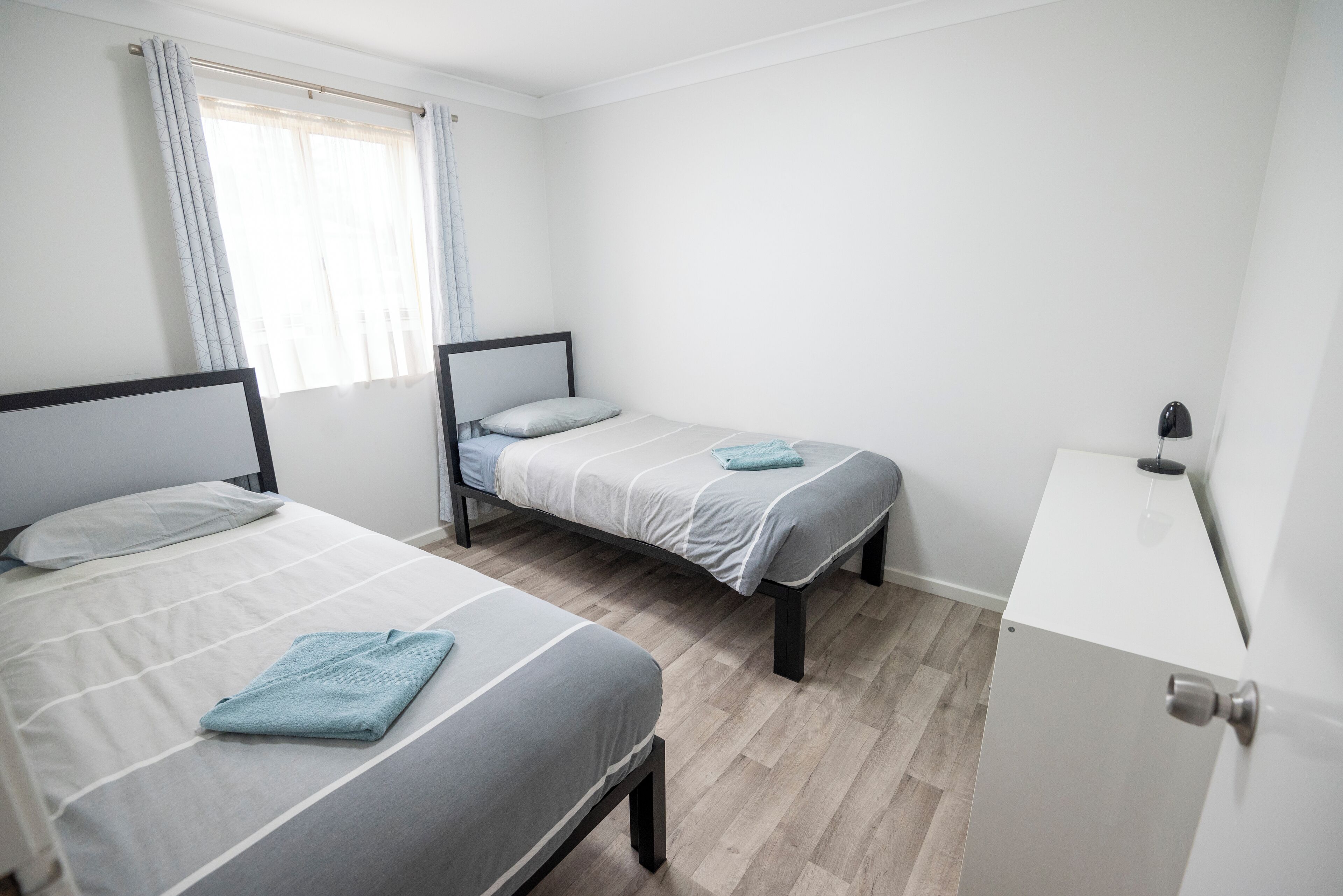 A room with two beds, a small desk, and a window with curtains.