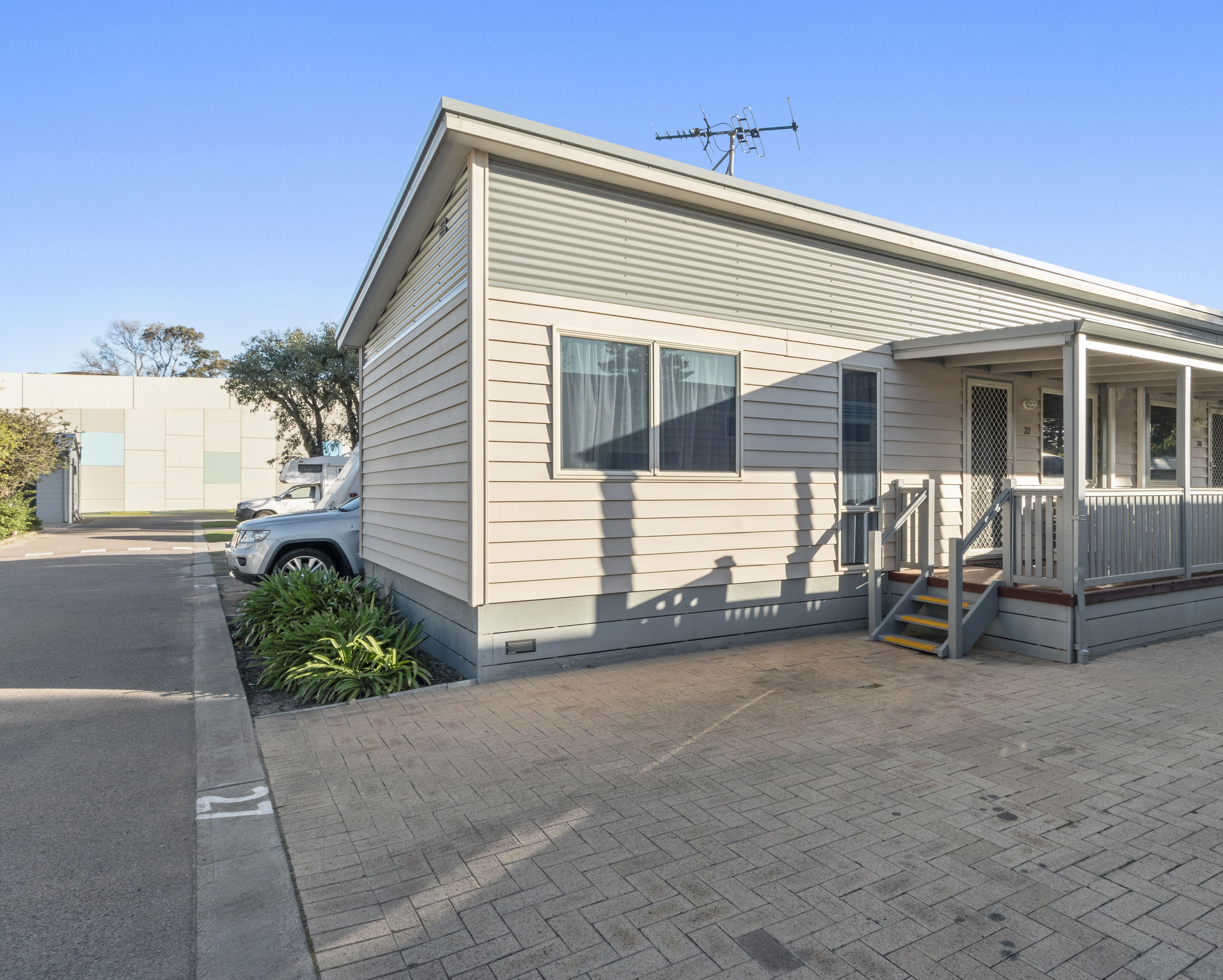 A single-story mobile home with a porch, a staircase, and a vehicle parked in front.