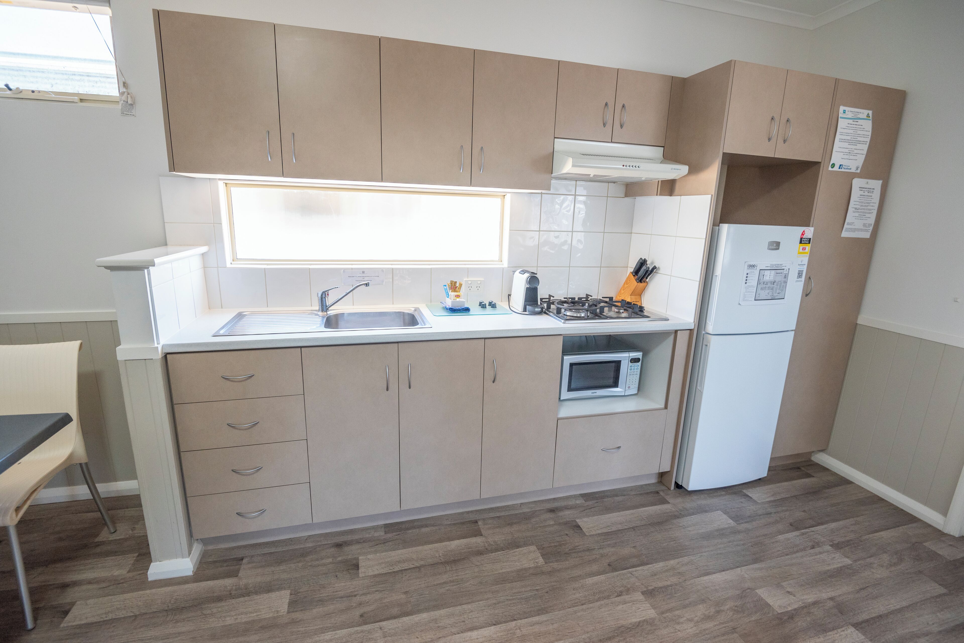 Een moderne keuken met beige kastjes, een wit aanrecht, een ingebouwde oven, een magnetron, een kookplaat en een koelkast.
