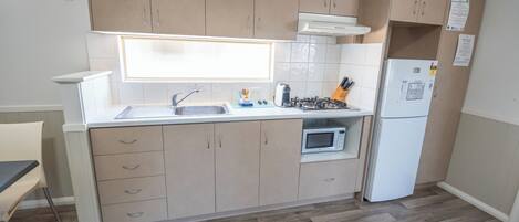 Een moderne keuken met beige kastjes, een wit aanrecht, een ingebouwde oven, een magnetron, een kookplaat en een koelkast.