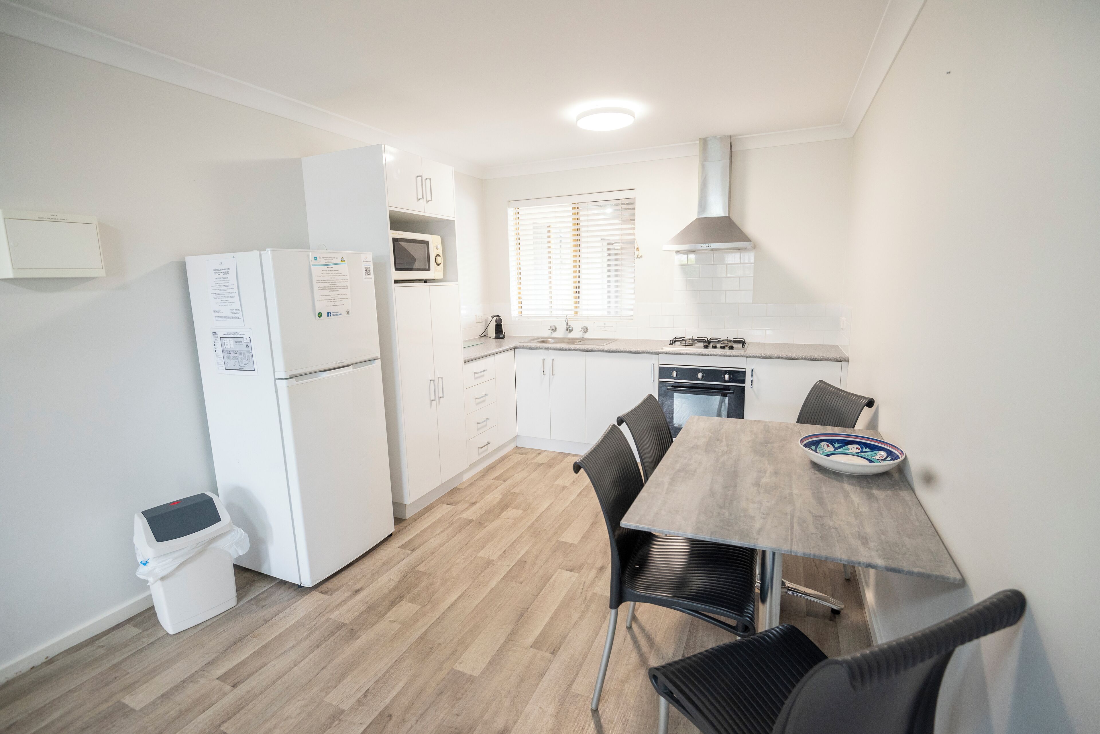 Een kleine keuken met een koelkast, magnetron, fornuis en een eettafel met stoelen.
