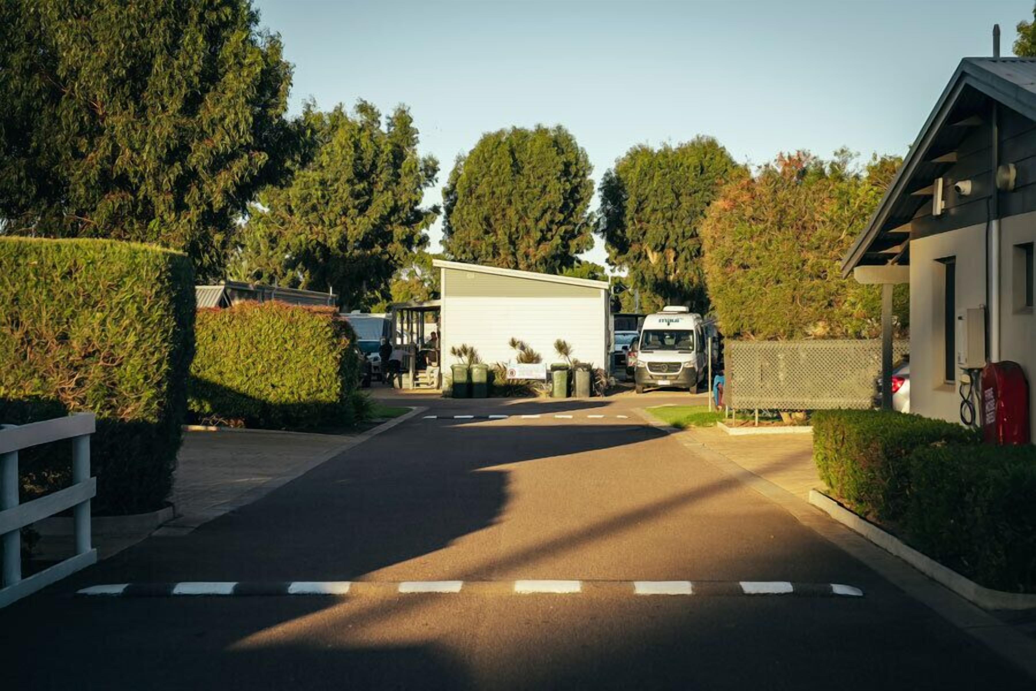 Une route menant à un bâtiment blanc doté d’un espace de stationnement couvert.