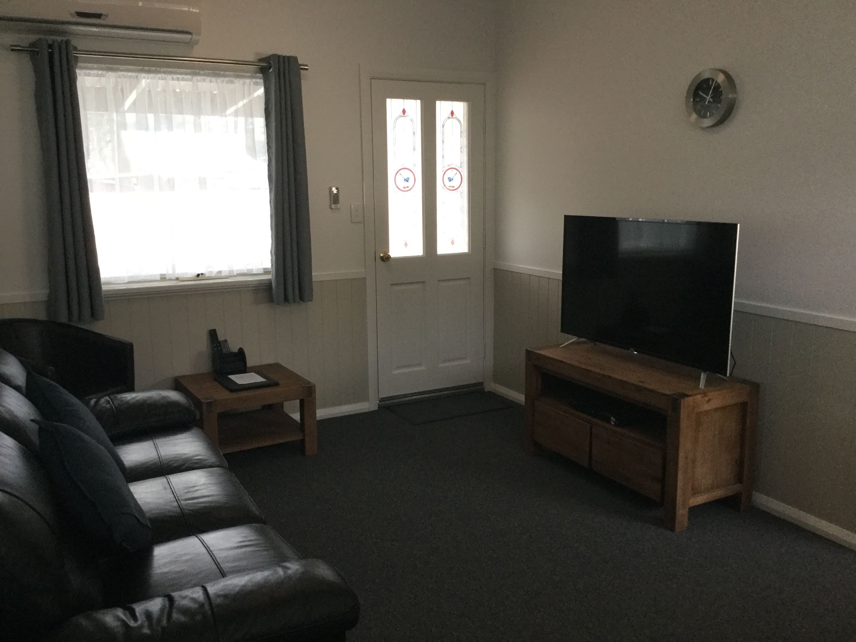 A living room with a leather sofa, a wooden coffee table, a flat-screen TV on a wooden stand, and a door with frosted glass panels.