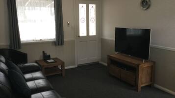 A living room with a leather sofa, a wooden coffee table, a flat-screen TV on a wooden stand, and a door with frosted glass panels.