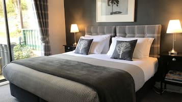 A neatly made bed with a grey and white checkered bedspread, two bedside lamps, and a framed artwork of a tree on the wall.
