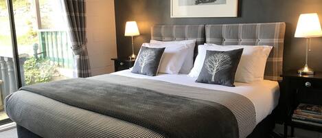 A neatly made bed with a grey and white checkered bedspread, two bedside lamps, and a framed artwork of a tree on the wall.