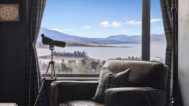 A room with a leather sofa, a telescope, and a view of mountains and a lake. - Troldhaugen Lodge - Adults Only (Jindabyne)