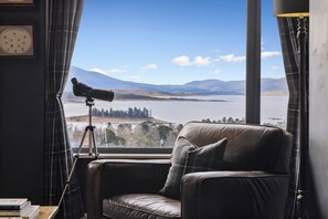 A room with a leather sofa, a telescope, and a view of mountains and a lake. - Troldhaugen Lodge - Adults Only (Jindabyne)
