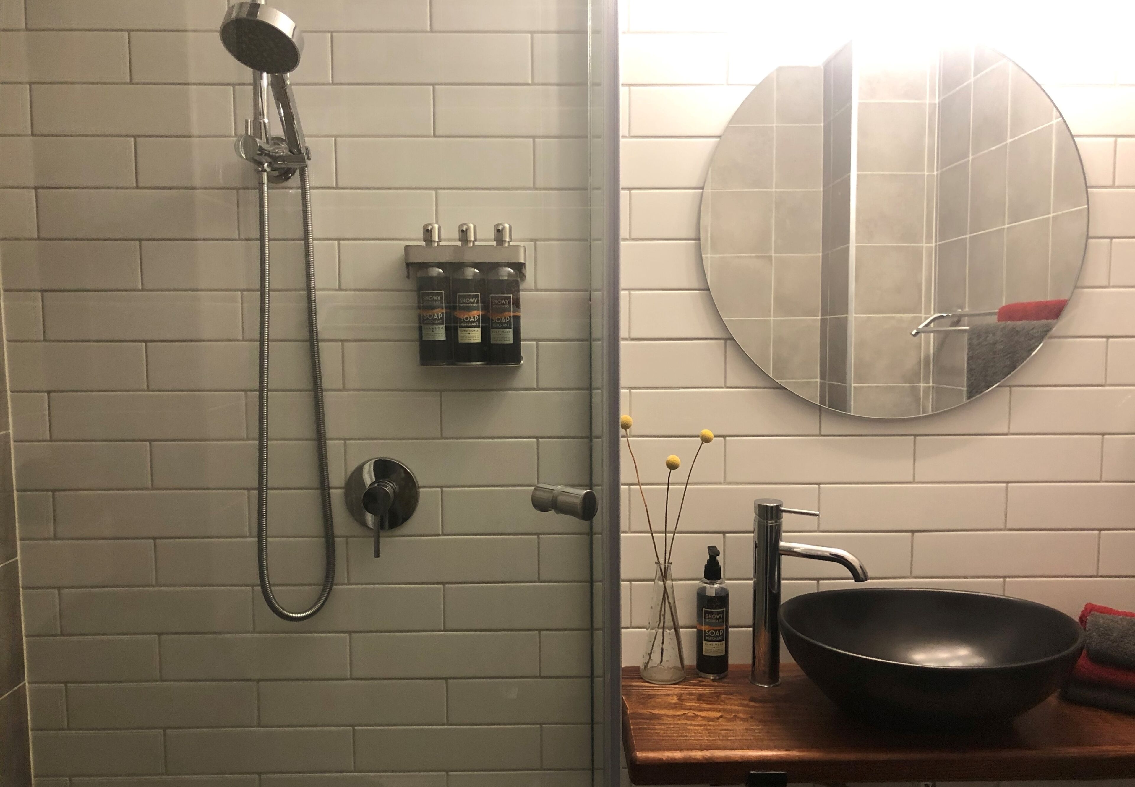 A bathroom with a shower, a sink with a large mirror, and toiletries on the wall.