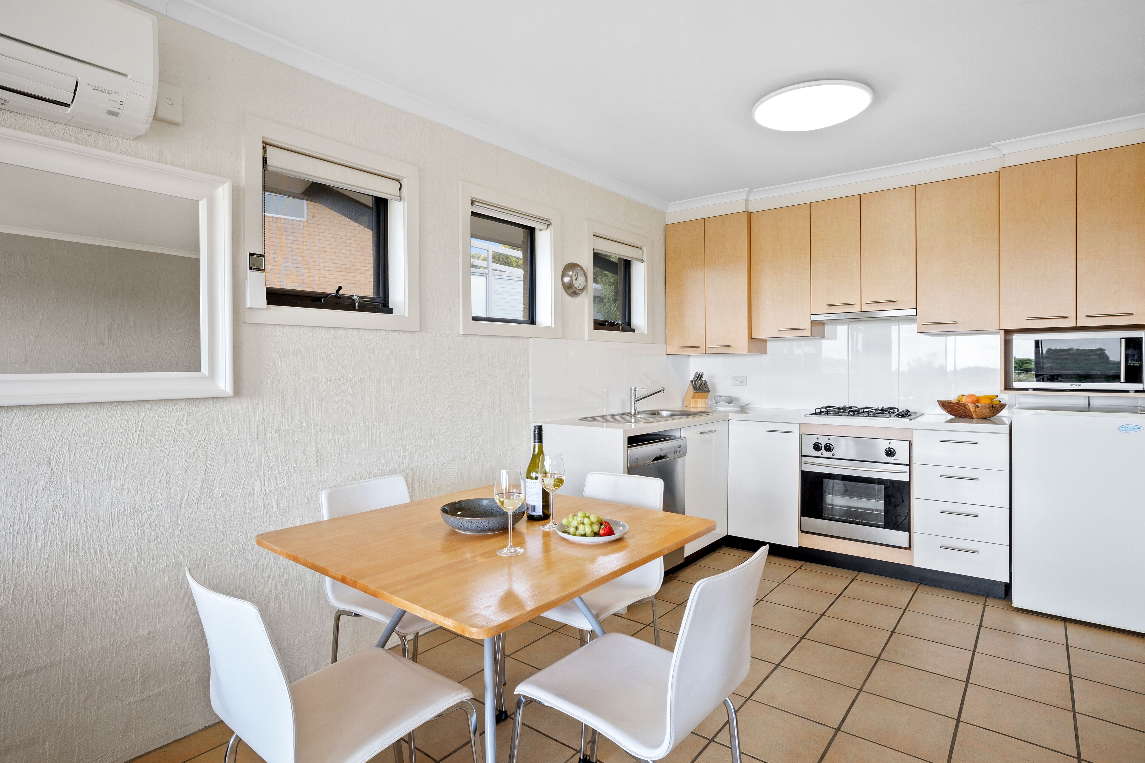 A modern kitchen with white cabinets, a wooden dining table, and a built-in oven.