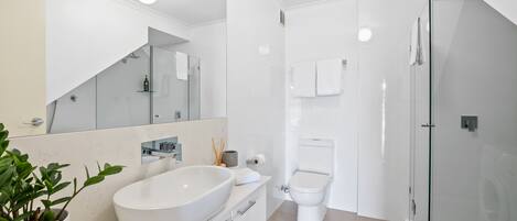 Ein modernes Badezimmer mit einem großen, weißen Waschbecken, einer Duschkabine aus Glas und einer Toilette.
