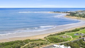 Vista aérea de una zona costera con playa arenosa, carretera y área residencial con casas y vegetación.