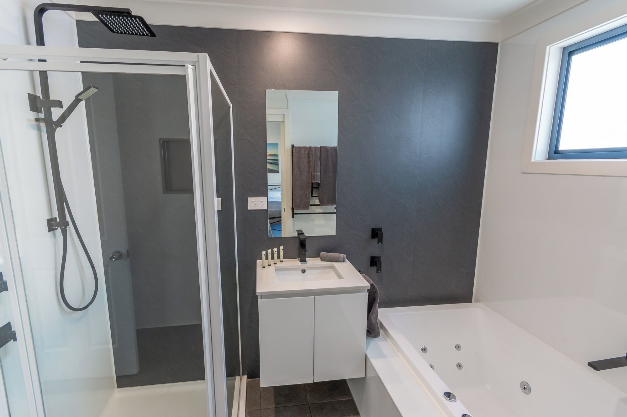 Un baño moderno con cabina de ducha de vidrio, tocador blanco con espejo y zona de bañera independiente.