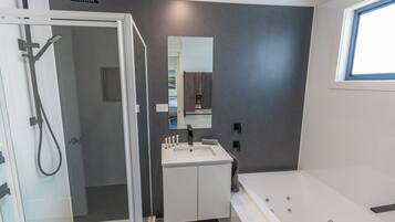 Un baño moderno con cabina de ducha de vidrio, tocador blanco con espejo y zona de bañera independiente.