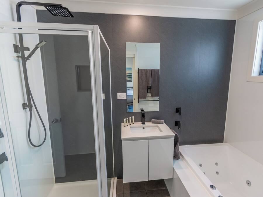 Un baño moderno con cabina de ducha de vidrio, tocador blanco con espejo y zona de bañera independiente.