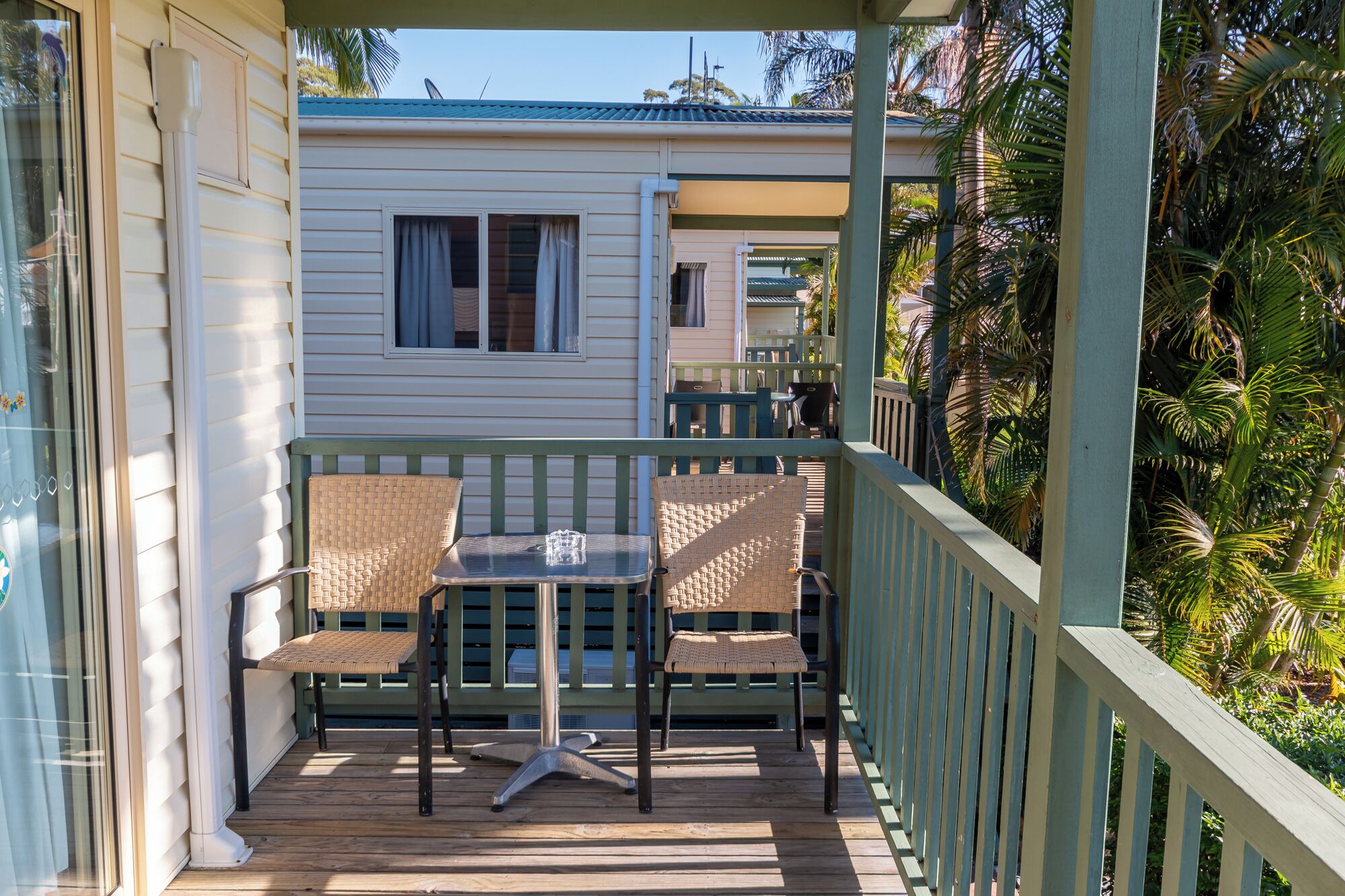 A covered outdoor area with two wicker chairs and a small table, surrounded by a wooden deck and a green railing.